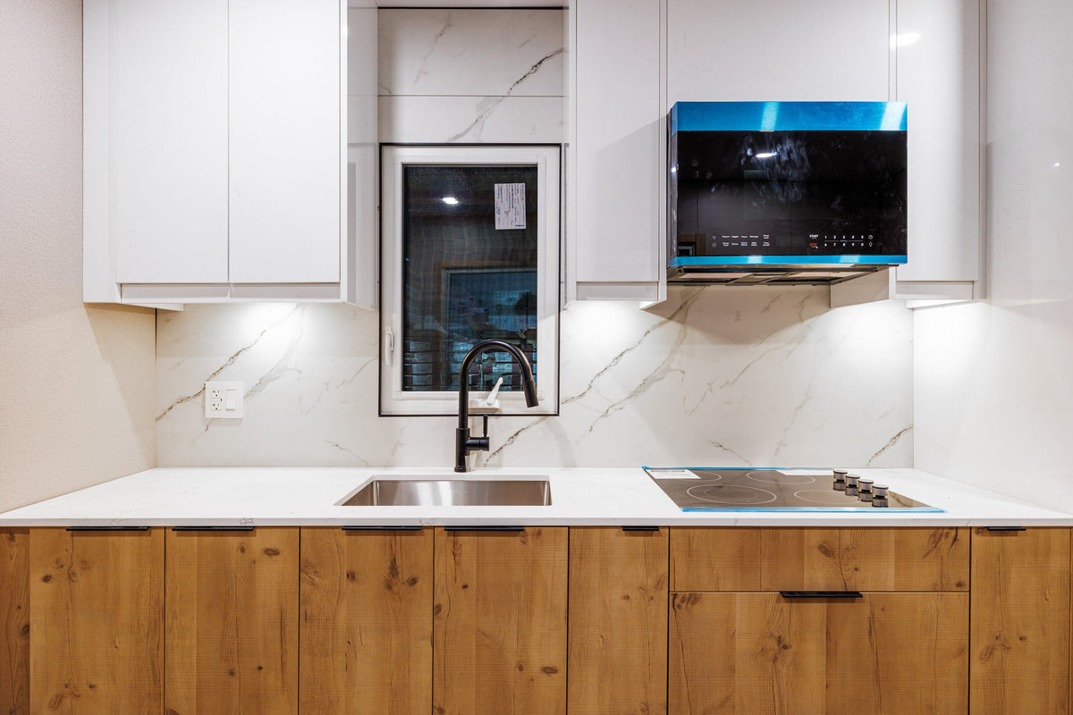 Exhibition kitchen display with white marble-look wall panels, white upper cabinets and wood-tone lower cabinets.