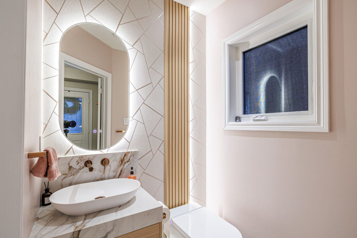 Newmarket powder room with an oval mirror, patterned wall and vertical accent beside a window.